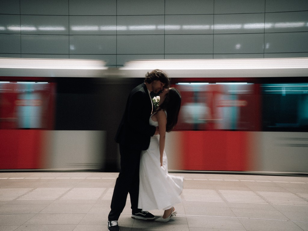 Bride and groom about to kiss on a subway platform, passing train motion-blurred