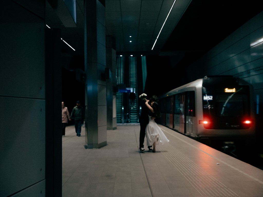 Bride and groom embracing on a subway platform beside a stopped train