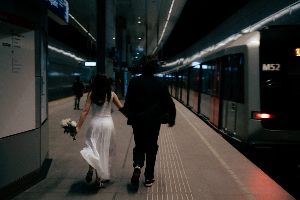 Bride and groom running along a subway platform away from camera, train alongside