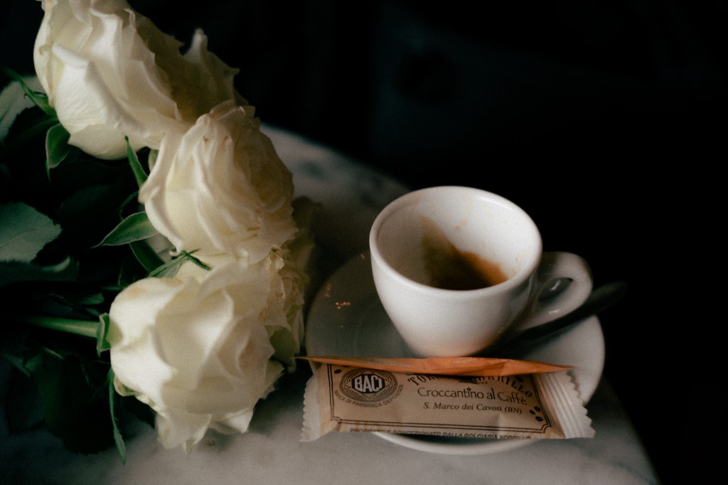 White roses on marble beside an empty espresso cup and a small wrapped treat